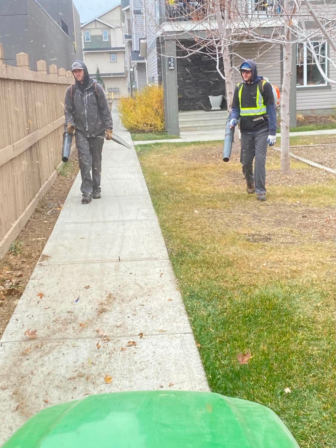 Two Phoenix Landscaping crew members walking a property with backpack blowers during a cleanup