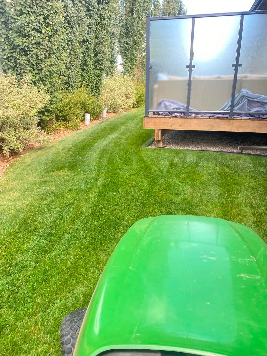 A neatly striped lawn beside a residential deck, freshly cut on a maintenance visit